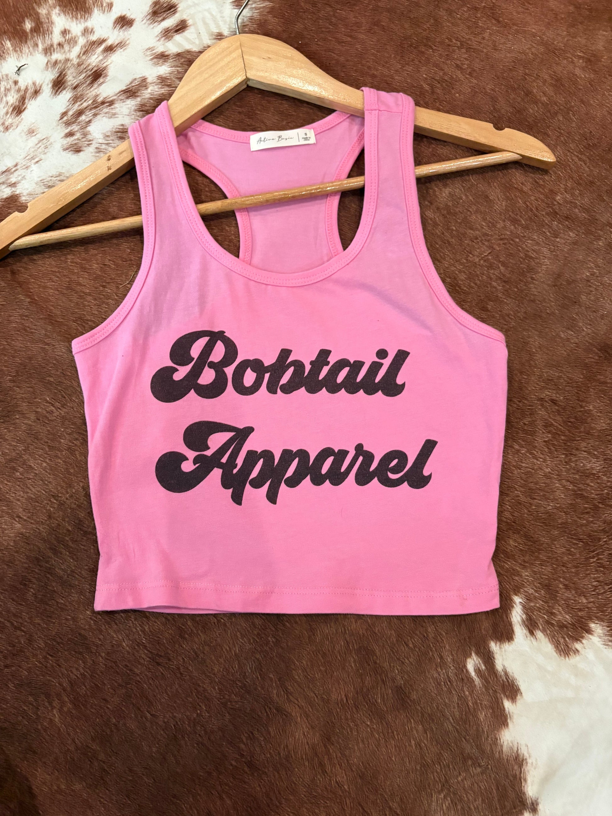 Pink tank top with 'Bobtail Apparel' text on a brown and white patterned surface